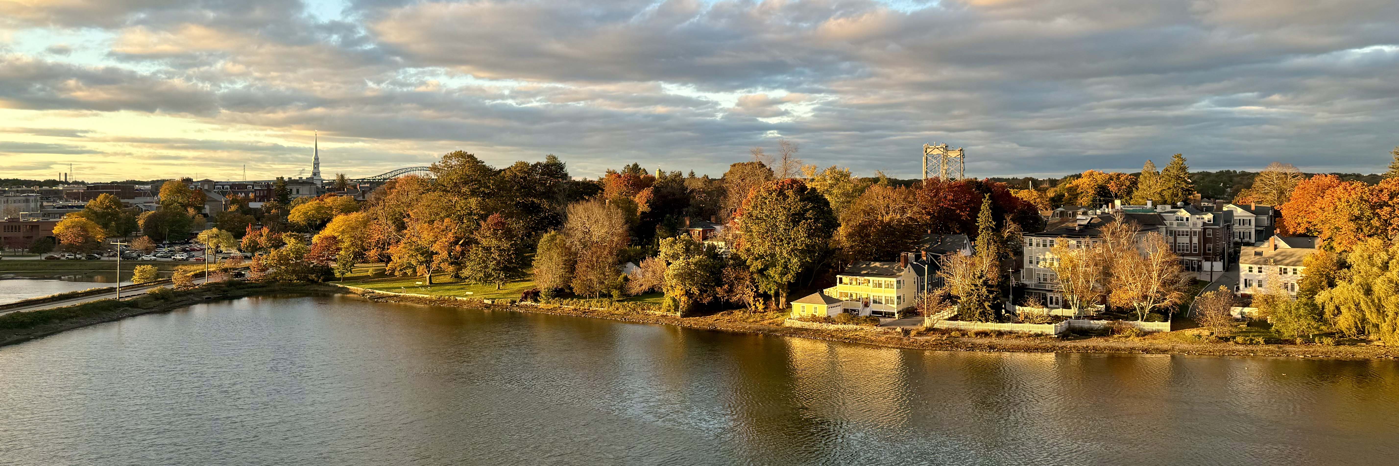picture of south mill pond at golden hour with the pond in the foreground, trees buildings, and bridges in the background