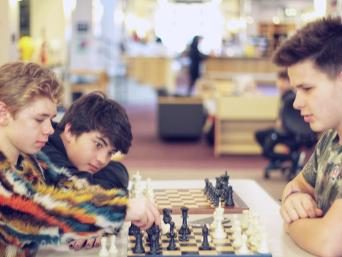 Three teenage boys playing chess