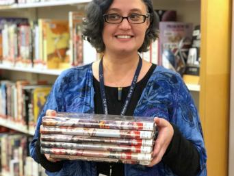 Library staff member with stack of graphic novels